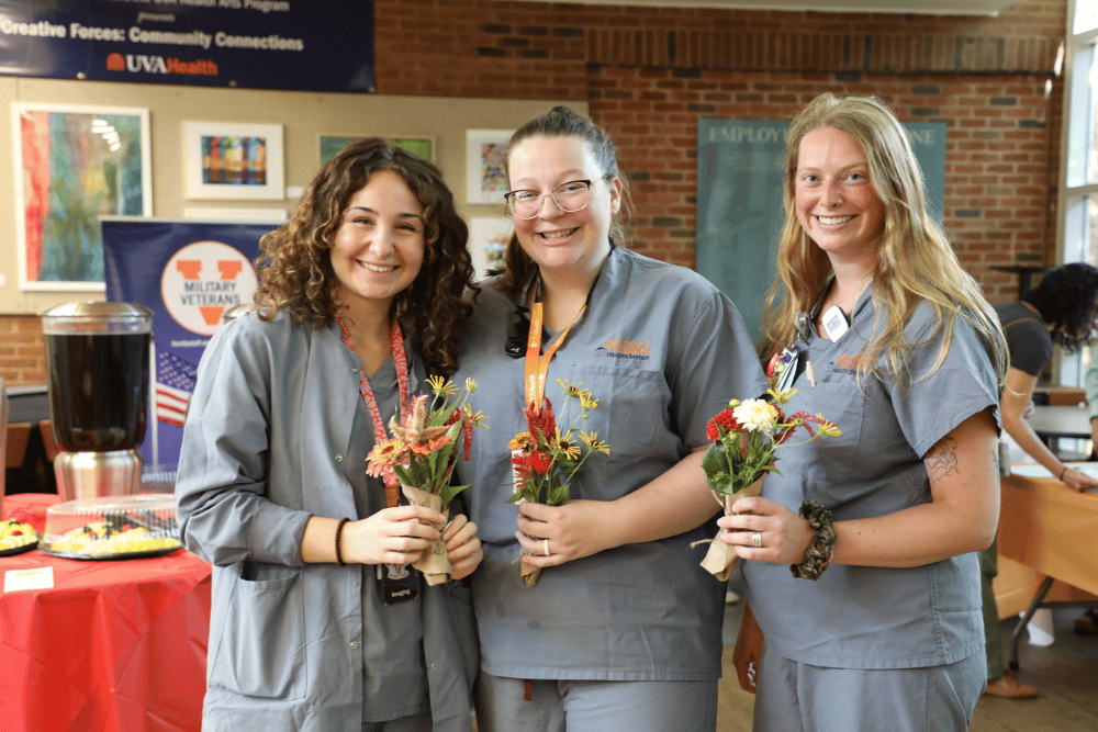 three hospital employees in scrubs stand smiling with flowers