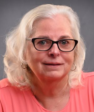 Emily Hauenstein's face and upper chest.  Emily has shoulder-length  silver hair, small hoop earrings, and glasses. She has a slight smile..