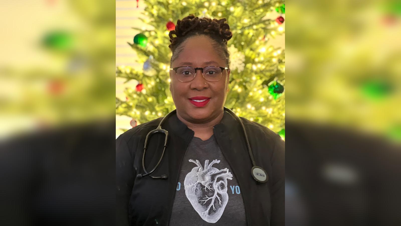 Princess Williams smiling with her nursing scrubs on in front of Christmas Tree