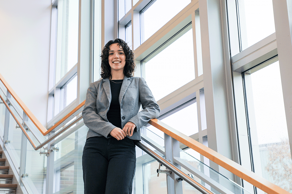 Reanna Panagides, Nursing PhD student, standing on stairs in front of large windows at the School of Nursing.
