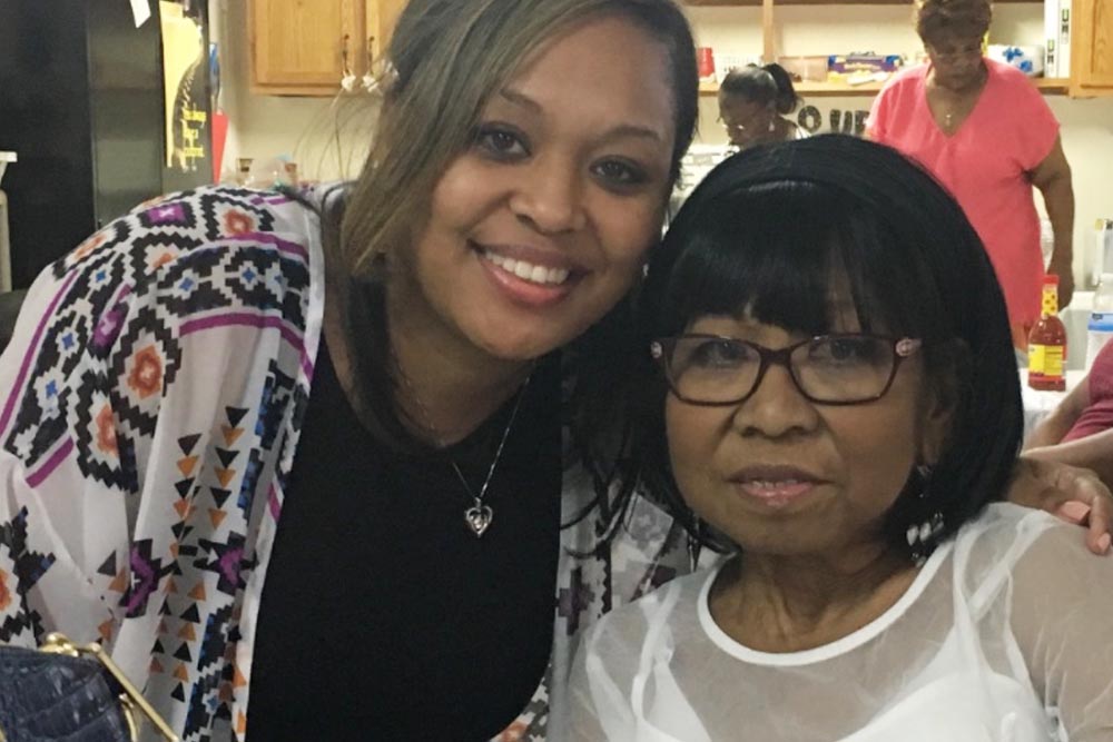 A mother and daughter stand together and smile.